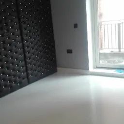 Jasnoszara, gładka posadzka w pokoju z czarną, pikowaną ścianą i oknem balkonowym.