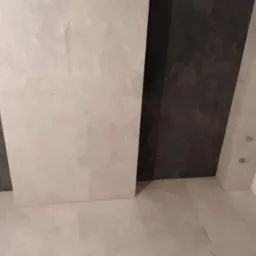 Wykończona łazienka z ciemnoszarą i beżową płytką na ścianach oraz podłodze, widoczny fragment brodzika z odpływem.