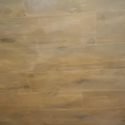 Ułożona podłoga z płytek imitujących drewno, widoczne fugi i naturalne odcienie brązu z delikatnymi ciemniejszymi przebarwieniami.