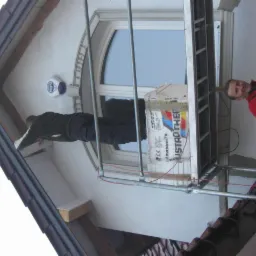 Prace ociepleniowe przy oknie na elewacji domu. Na rusztowaniu materiały izolacyjne, pracownik w trakcie montażu. Widok z dołu na elewację.