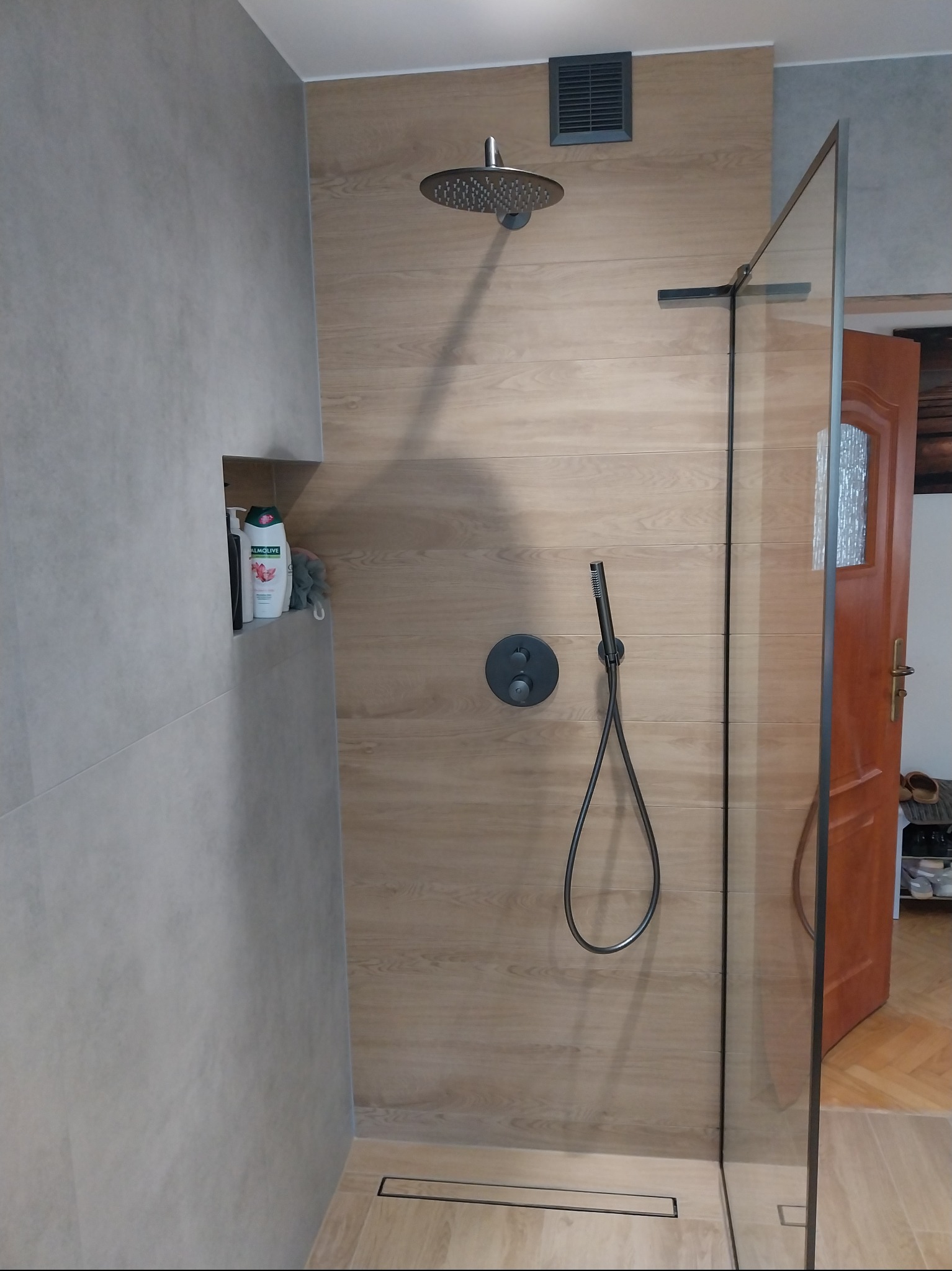 Nowoczesna kabina prysznicowa walk-in z deszczownicą i panelami imitującymi drewno. Minimalistyczny design, szklana ściana, odpływ liniowy w podłodze.