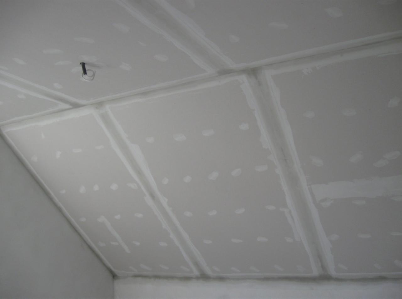 Sufit z płyt kartonowo-gipsowych, łączenia zaszpachlowane, widoczne wkręty. Etap prac wykończeniowych, przygotowanie do malowania. Neutralne oświetlenie.