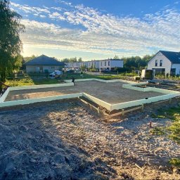 MAX PROJEKT SPÓŁKA Z OGRANICZONĄ ODPOWIEDZIALNOŚCIĄ - Fundamenty domu jednorodzinnego w trakcie budowy, ocieplone styropianem, widok z góry na plac budowy w słoneczny dzień. W tle zabudowa jednorodzinna i drzewa.