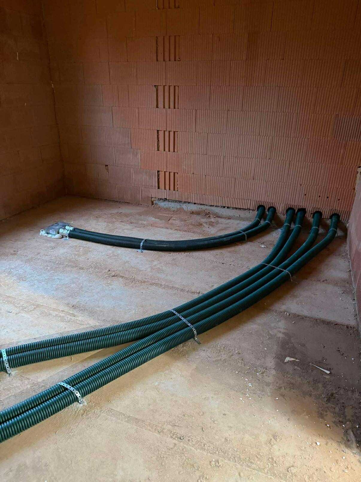 Zielone rury wentylacyjne przymocowane do ściany z cegły dziurawki, ułożone na surowej podłodze. Instalacja rekuperacji w trakcie montażu.