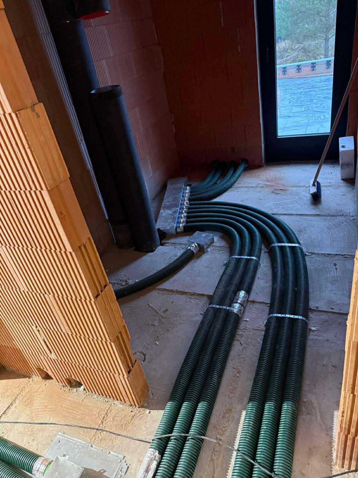 Instalacja rekuperacji podłogowej w surowym wnętrzu domu w Henrykowie-Uroczem. Widoczne rury wentylacyjne i rozdzielacz. Ściany z cegły dziurawki.