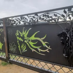 Metalowa brama wjazdowa z wycinanymi laserowo wzorami jelenia, wilka i motywami roślinnymi, wykończona w czarnym macie.