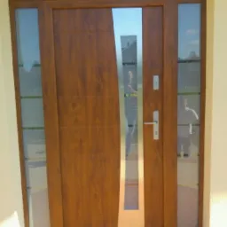 Nowoczesne drzwi wejściowe z drewnopodobnym wykończeniem i pionowym przeszkleniem, zamontowane w Pszowie, z bocznymi panelami szklanymi.