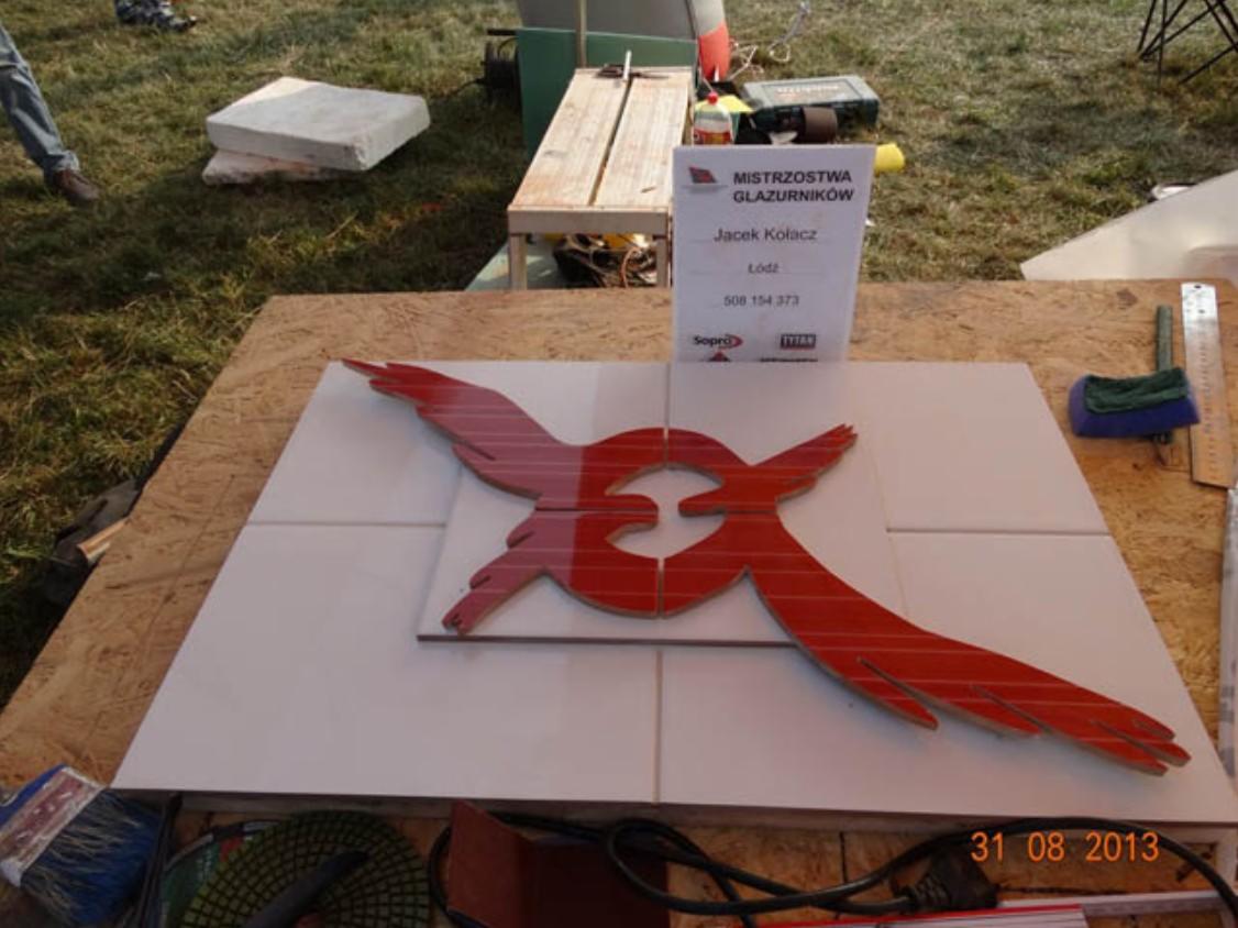 Kompozycja z białych płytek z czerwonym, błyszczącym logo w kształcie ptaka, prezentowana na tle tabliczki informacyjnej 'Mistrzostwa Glazurników' z datą 31.08.2013.