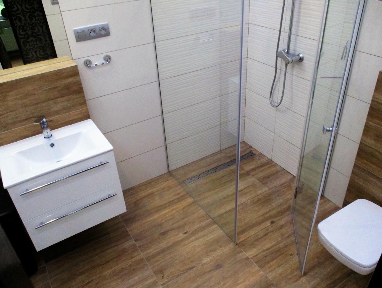 Wykończona łazienka w Łodzi z kabiną prysznicową, umywalką z szafką i toaletą, wyłożona płytkami imitującymi drewno na podłodze i ścianach.