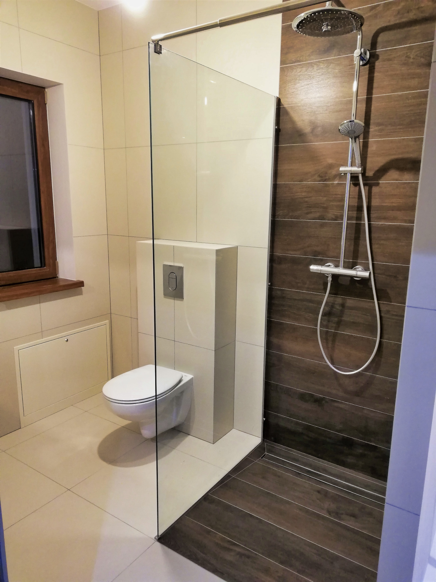 Nowoczesna łazienka z kabiną prysznicową typu walk-in, wiszącą toaletą i brązowymi płytkami imitującymi drewno pod prysznicem.