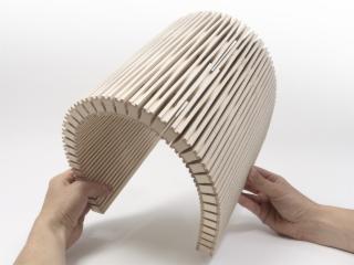 Elastyczny panel z cienkich, drewnianych listewek, wygięty w łuk i trzymany w dłoniach na białym tle.