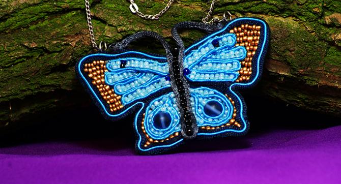 Ręcznie robiony wisiorek motyl z niebieskich i złotych koralików, wykonany techniką sutasz i wire-wrapping, na fioletowym tle i kawałku kory.