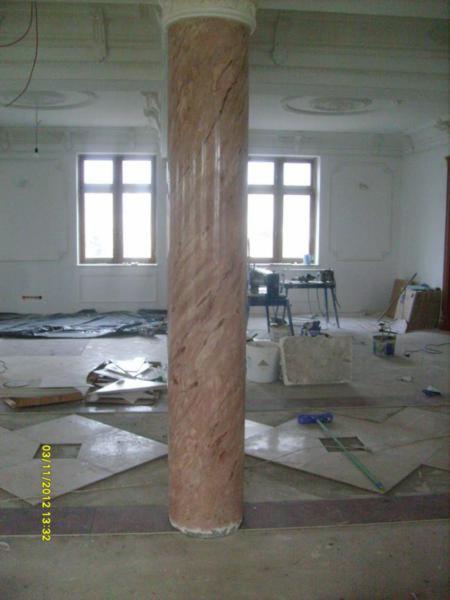 Kolumna dekoracyjna z efektem marmuru w trakcie prac wykończeniowych, widoczne płytki podłogowe i narzędzia.