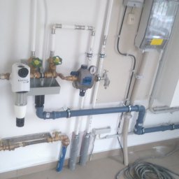 Instal-Mat - Złożona instalacja hydrauliczna z filtrem Artica, rurami PCV i miedzianymi zaworami, zamontowana na białej ścianie w Bielsku-Białej. Widoczne liczne złączki i mocowania.