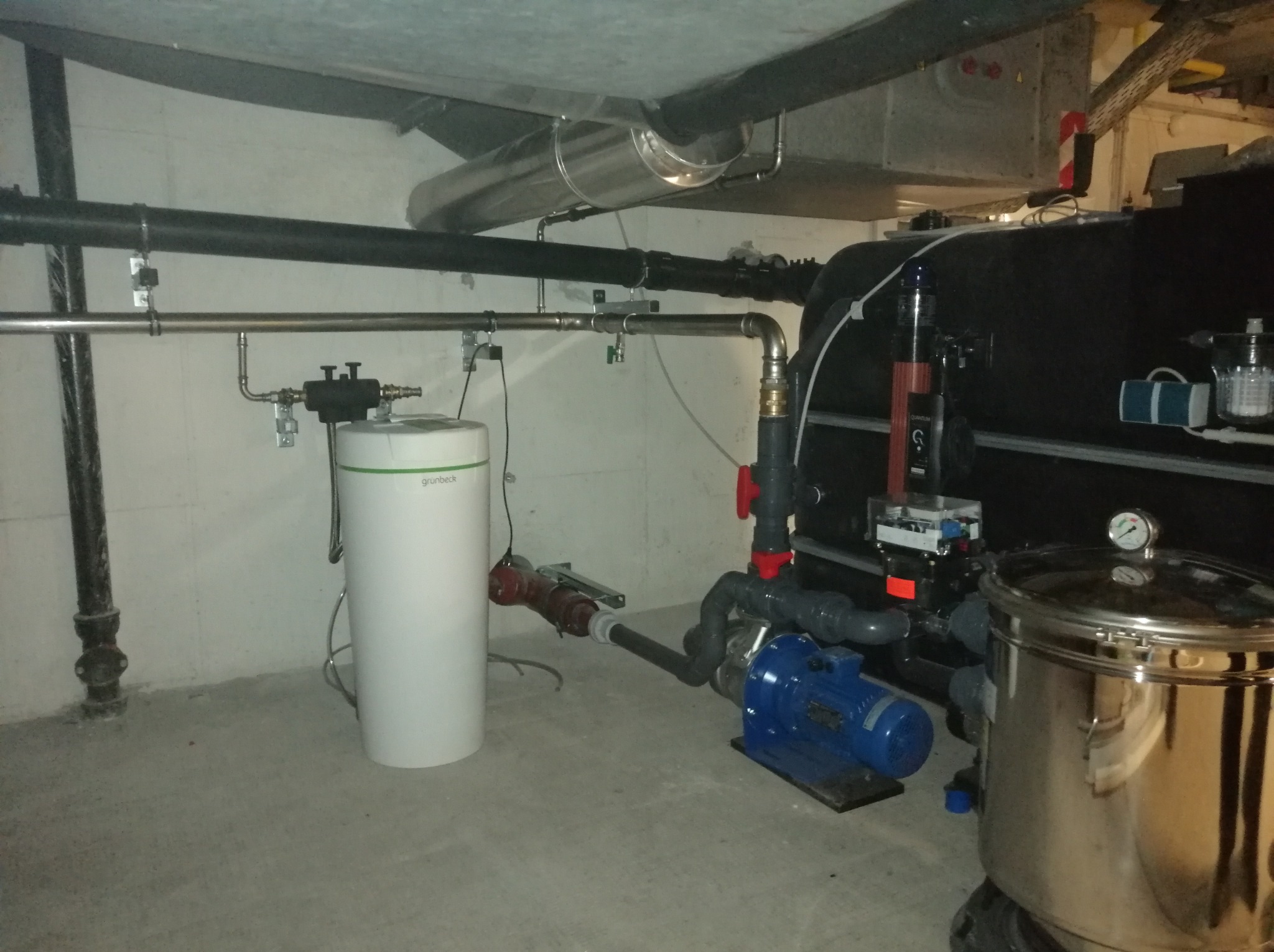Kotłownia: biały zbiornik wyrównawczy Grubeck, niebieska pompa obiegowa, stalowy filtr i rury instalacji centralnego ogrzewania w pomieszczeniu technicznym.