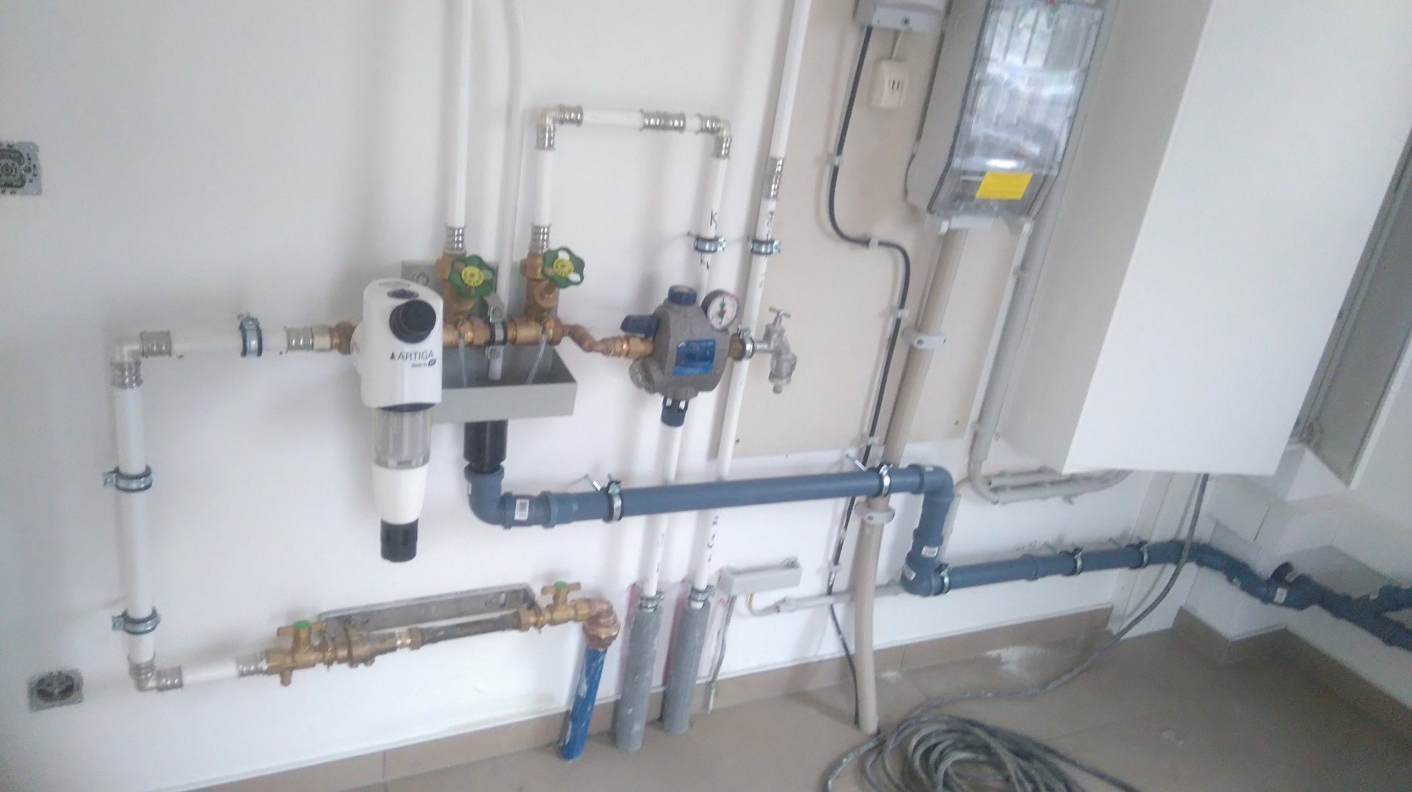 Złożona instalacja hydrauliczna z filtrem Artica, rurami PCV i miedzianymi zaworami, zamontowana na białej ścianie w Bielsku-Białej. Widoczne liczne złączki i mocowania.