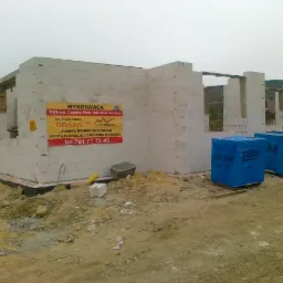 Wznoszenie ścian domu z bloczków SILKA, widoczne trzy opakowania bloczków SILKA w niebieskiej folii, na ścianie budynku baner reklamowy firmy budowlanej.