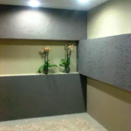 Nowoczesne wnętrze z dekoracyjną ścianą w odcieniach szarości i beżu, oświetleniem punktowym i dwoma storczykami w szklanych wazonach na półce.