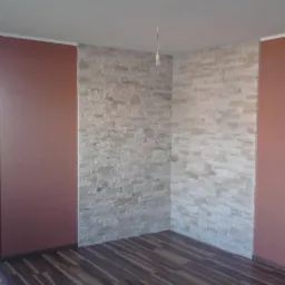 Pokój po odświeżeniu: ściany w kolorze terakoty i z dekoracyjną okładziną kamienną, ciemna podłoga imitująca drewno, widoczne przewody elektryczne wystające ze ściany.