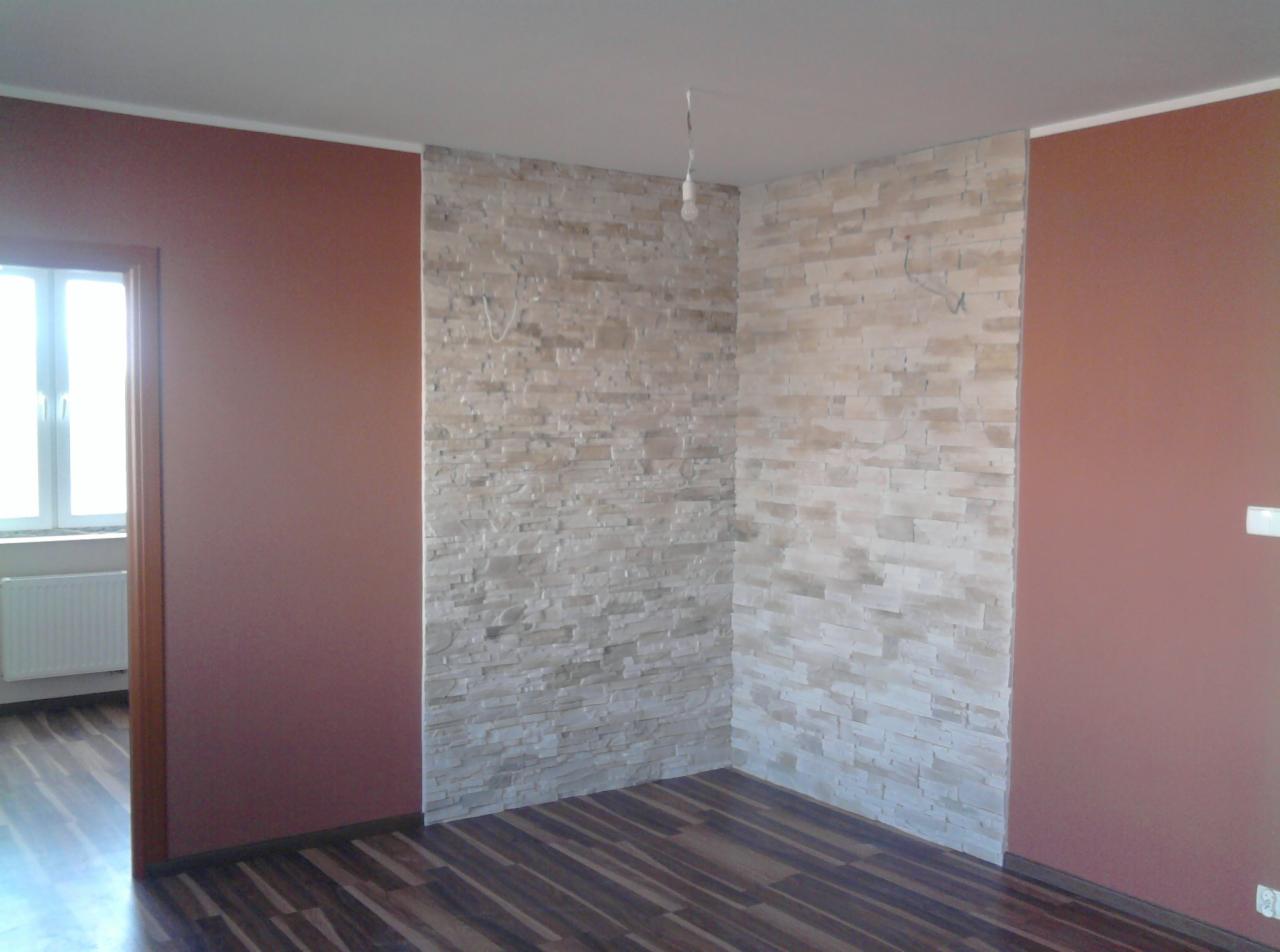 Pokój po odświeżeniu: ściany w kolorze terakoty i z dekoracyjną okładziną kamienną, ciemna podłoga imitująca drewno, widoczne przewody elektryczne wystające ze ściany.