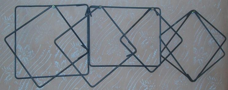 Cztery strzemiona zbrojeniowe o kwadratowym kształcie połączone ze sobą, wykonane z drutu stalowego, widoczne ślady spawania na łączeniach, tło w kolorze beżowym z delikatnym wzorem.