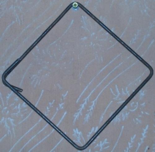 Kwadratowy strzemiączek zbrojeniowy z drutu żebrowanego, zawieszony na wkręcie na tle ściany z dekoracyjnym wzorem. Zagięte końce drutu widoczne w lewym dolnym rogu.