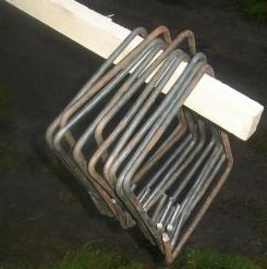 Stos strzemion zbrojeniowych w kształcie rombu, spiętych deską, leżących na ziemi.