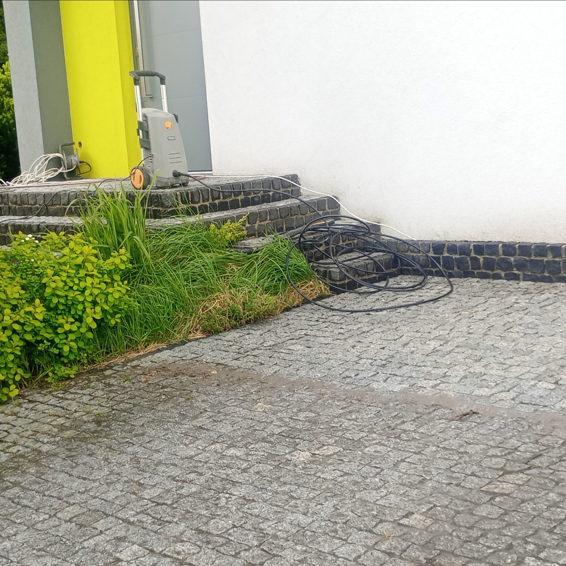 Czyszczenie kostki granitowej przy schodach wejściowych za pomocą myjki ciśnieniowej. Widoczna kostka, schody z kamienia i myjka ciśnieniowa.