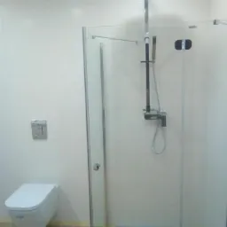 Nowoczesna kabina prysznicowa z deszczownicą i toaletą podwieszaną w wykończonej łazience z jasnymi płytkami.