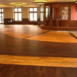 Duża sala z dekoracyjną podłogą z ciemnego i jasnego drewna, z krzesłami odwróconymi do góry nogami na barze i sofą w tle.