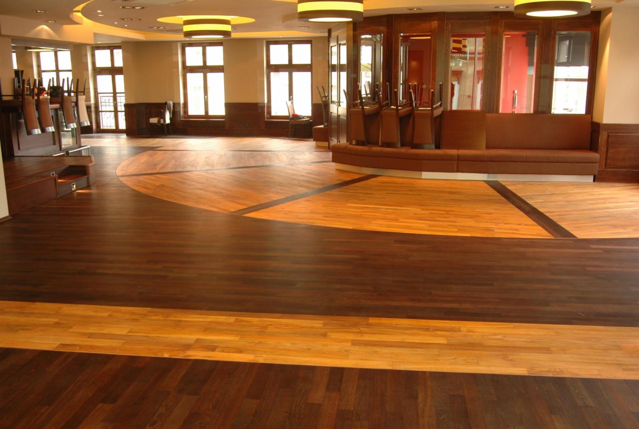 Duża sala z dekoracyjną podłogą z ciemnego i jasnego drewna, z krzesłami odwróconymi do góry nogami na barze i sofą w tle.