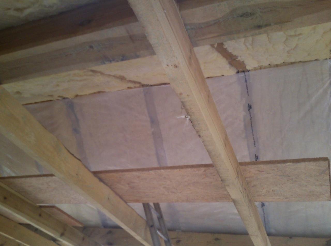 Izolacja poddasza z widoczną wełną mineralną i folią paroizolacyjną, drewniana konstrukcja więźby dachowej, widok z dołu.