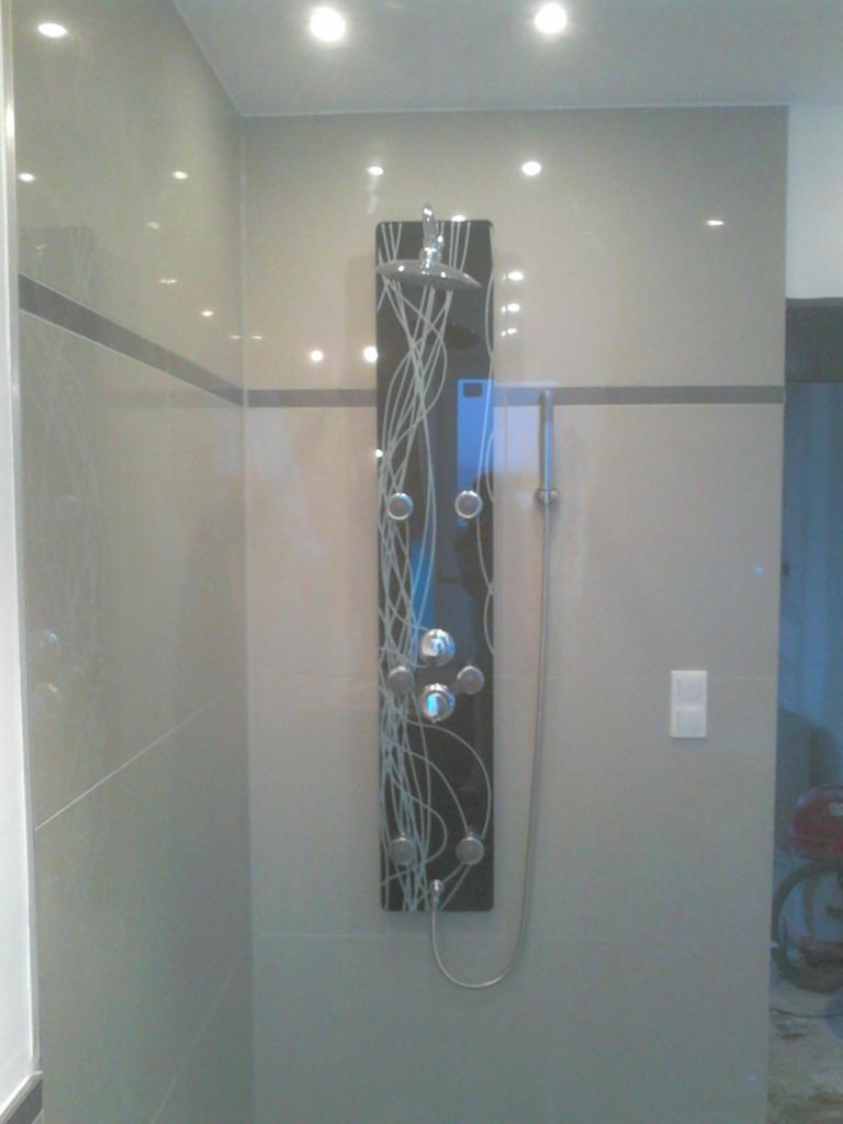 Nowoczesny panel prysznicowy z hydromasażem, zamontowany na ścianie z jasnych płytek. Widoczne elementy instalacji i oświetlenie punktowe.