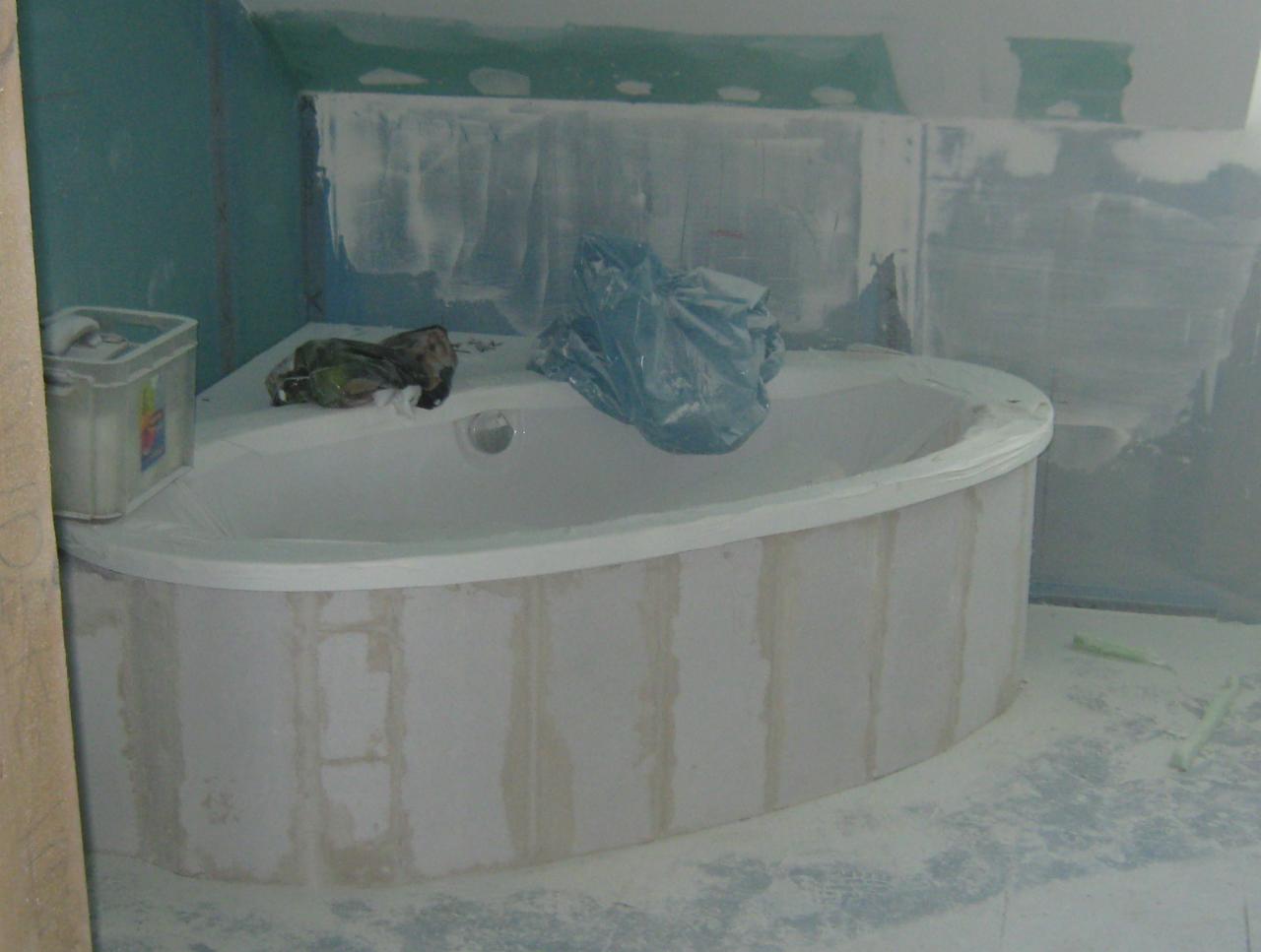 Narożna wanna obudowana płytami gipsowymi, przygotowana do wykończenia w łazience. Widoczne ślady gładzi na wannie i podłodze.