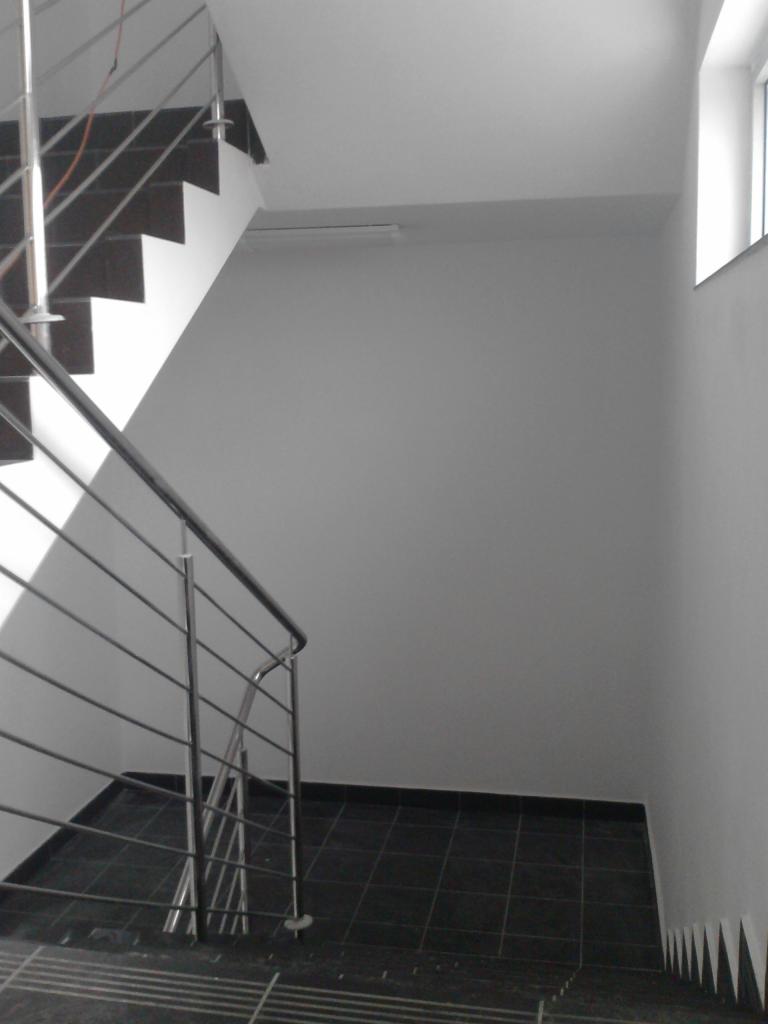 Schody wewnętrzne z czarną terakotą, metalowa balustrada, świeżo pomalowane białe ściany i sufit, widok z góry na dół.
