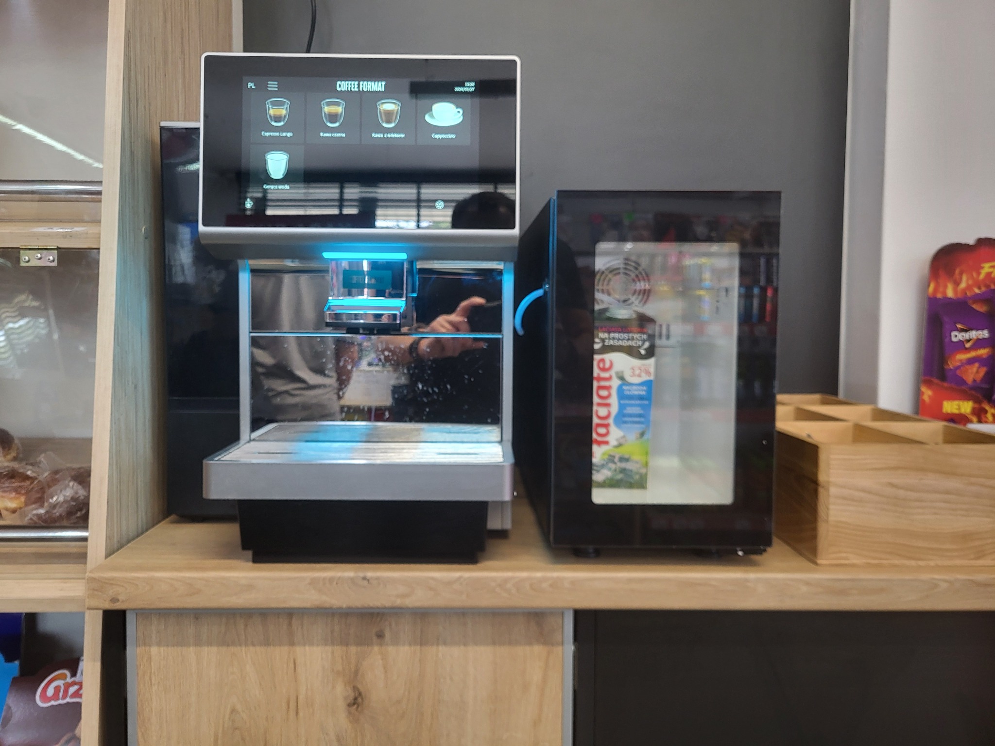 Automatyczny ekspres do kawy z chłodziarką na mleko w biurze, widoczny panel dotykowy z wyborem rodzaju kawy.