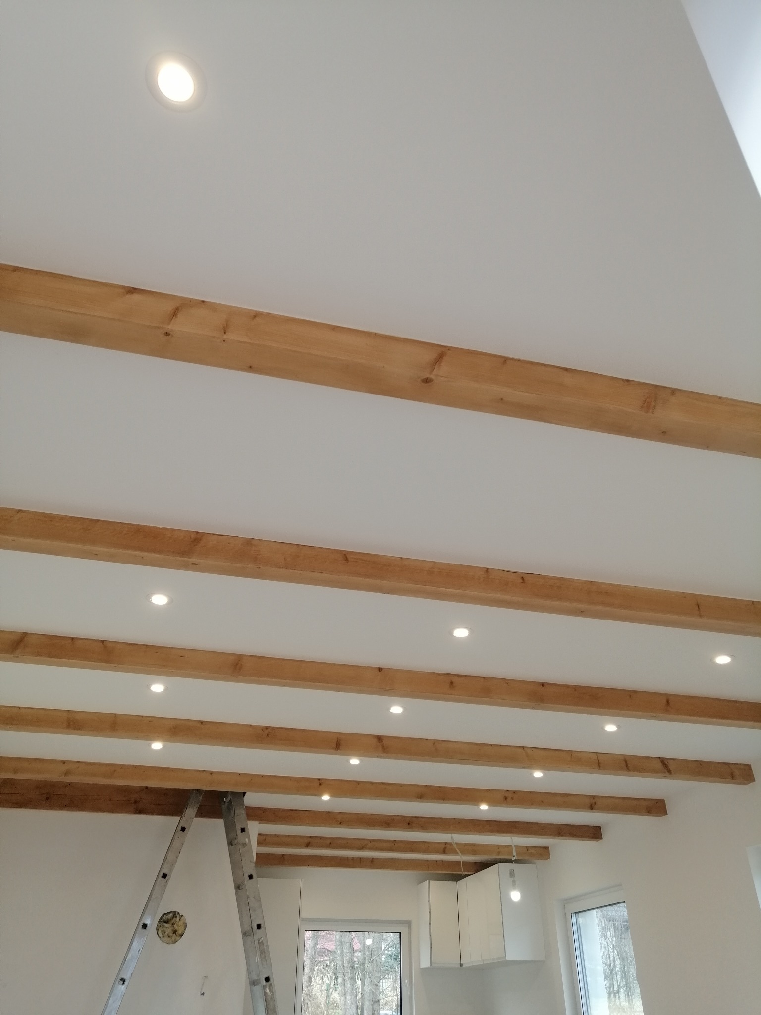 Sufit z drewnianymi belkami i zamontowanym oświetleniem punktowym w Radziechowach, widoczna drabina i fragment zabudowy kuchennej.