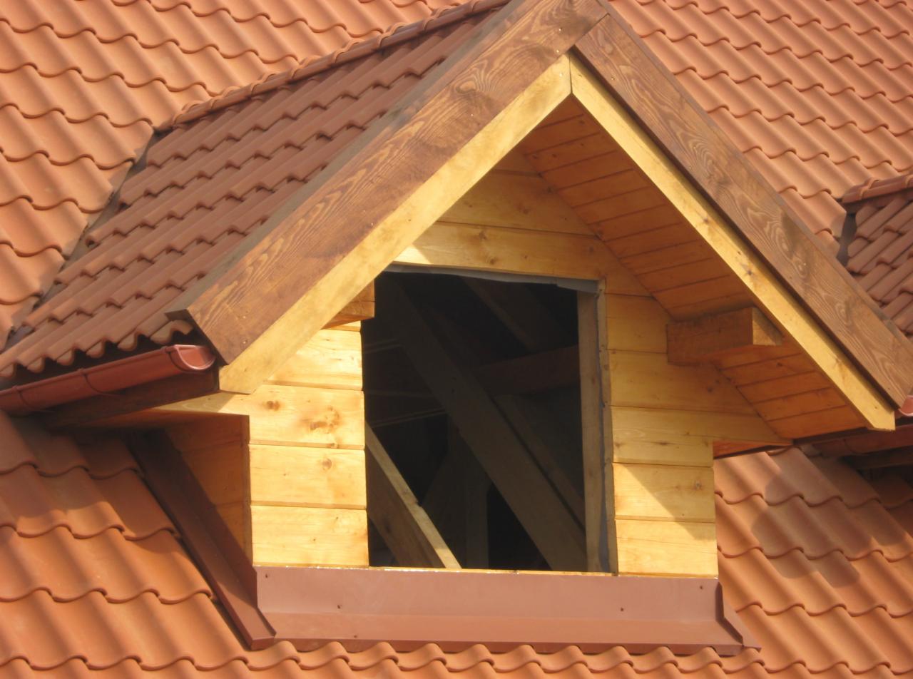 Drewniana lukarna w dachu z czerwonej dachówki ceramicznej, widok z bliska. Widoczne detale konstrukcyjne i orynnowanie. Jasne, naturalne światło.