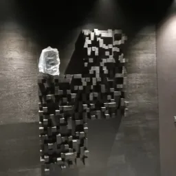 Montaż dekoracyjnej ściany z drewnianych kostek w ciemnym wnętrzu, zabezpieczona folią, oświetlenie punktowe.