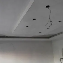 Szpachlowana sufitowa konstrukcja z wywierconymi otworami na oświetlenie, widoczne przewody, wstępnie przygotowane ściany do dalszych prac wykończeniowych.