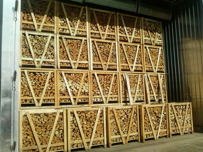 Kilkanaście drewnianych skrzyń wypełnionych pociętym drewnem, ułożonych wewnątrz metalowej naczepy transportowej. Drewno ułożone równo w skrzyniach.