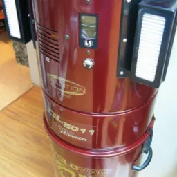 Cylindryczny odkurzacz centralny Cyclovac DL-5011 w kolorze bordowym, z panelem sterowania i filtrami na bokach, widoczne logo i model.