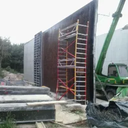 Wznoszenie ścian z szalunków systemowych, widoczny dźwig i rusztowanie na placu budowy w pochmurny dzień.