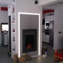 Nowoczesny salon z kominkiem obudowanym w szarą ścianę z podświetleniem LED, widoczne drewno do kominka i fragment kuchni w tle.