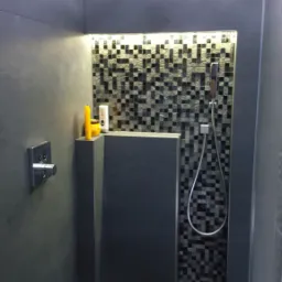 Nowoczesna kabina prysznicowa z szarymi płytkami, mozaiką w strefie prysznica i deszczownicą, oświetleniem LED oraz widocznymi kosmetykami na półce.