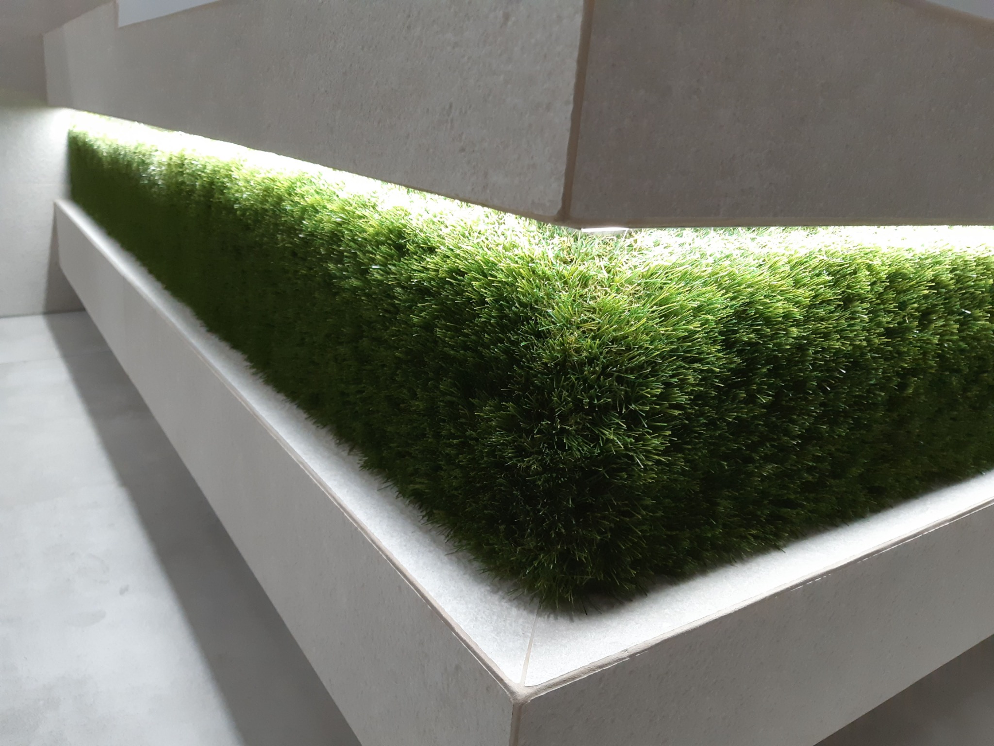 Dekoracyjna ściana z sztucznej trawy podświetlona od góry, tworząca nowoczesny element wystroju wnętrza.