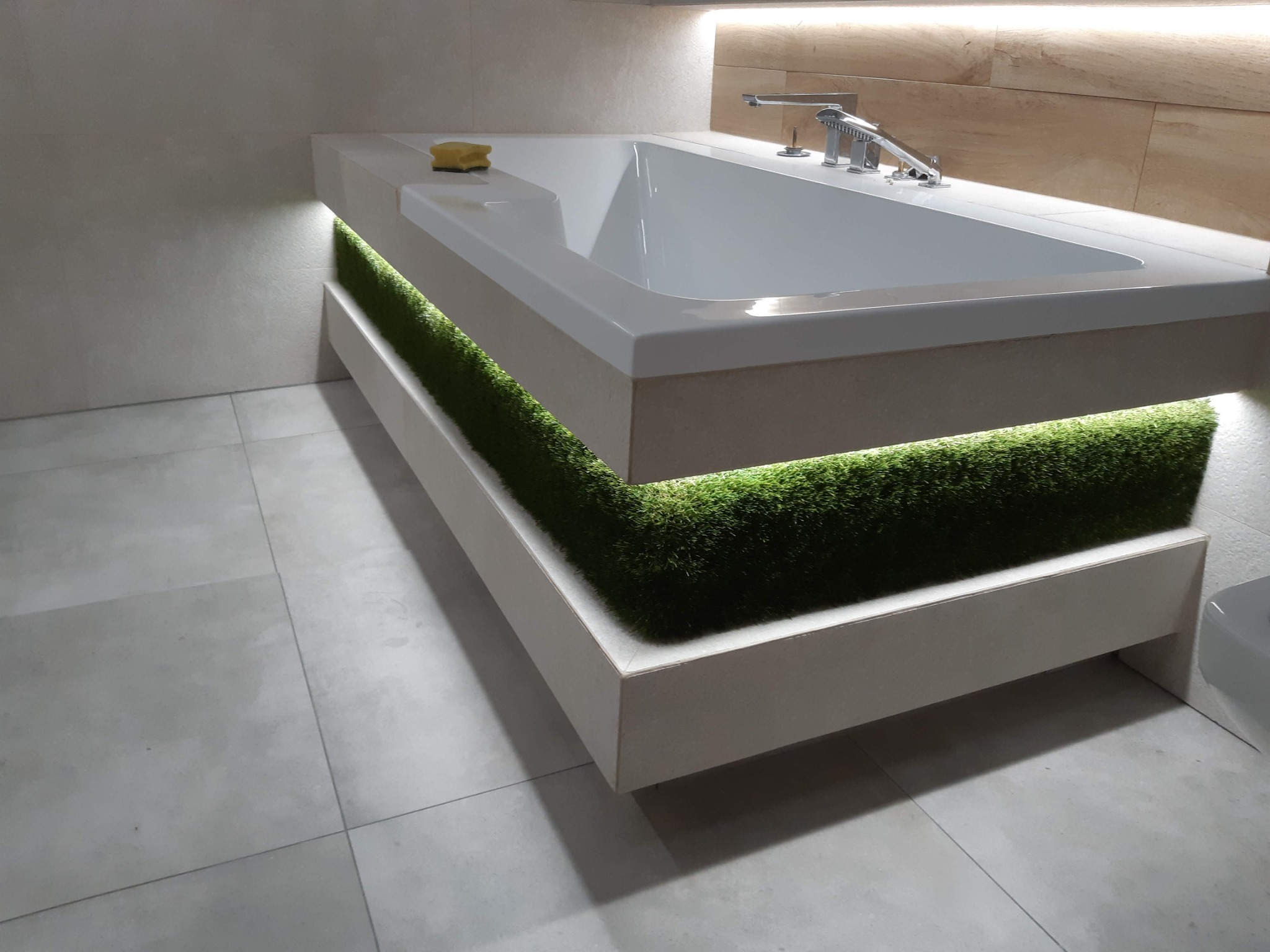 Nowoczesna wanna z podświetlaną zieloną dekoracją imitującą trawę, minimalistyczna armatura, jasne płytki i oświetlenie LED w łazience.