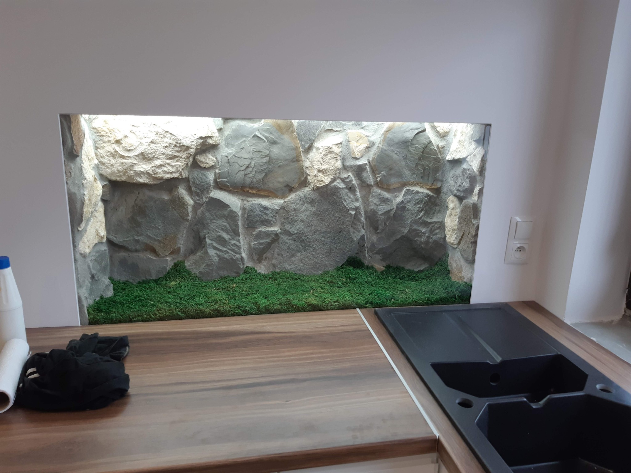 Nietypowa aranżacja łazienki: kamienna ściana z mchem wnęce nad blatem z czarnym zlewem, widok z bliska.