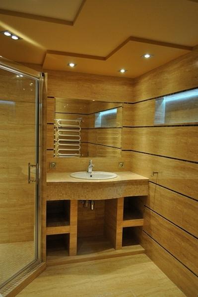 Jasna łazienka wykończona trawertynem z kabiną prysznicową, umywalką wpuszczoną w blat i podświetlanym lustrem.