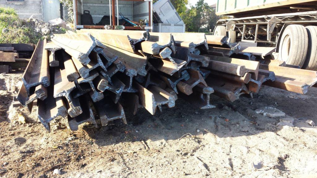 Stalowe szyny S49 ułożone na ziemi, widoczny fragment ciężarówki w tle.